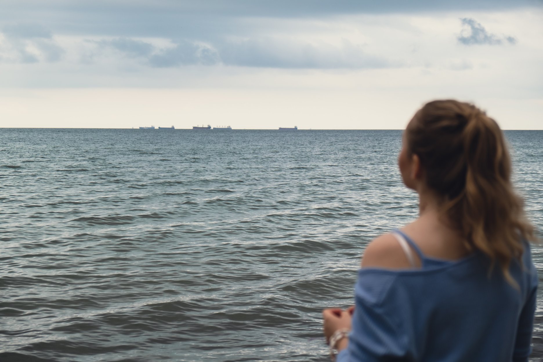 Defocused Young woman standing back on blurred beachside background. Attractive female enjoying walking the sea shore. travel and active lifestyle concept. Springtime. Relaxation, youth, love, lifestyle solitude with nature. Wellness wellbeing mental heal